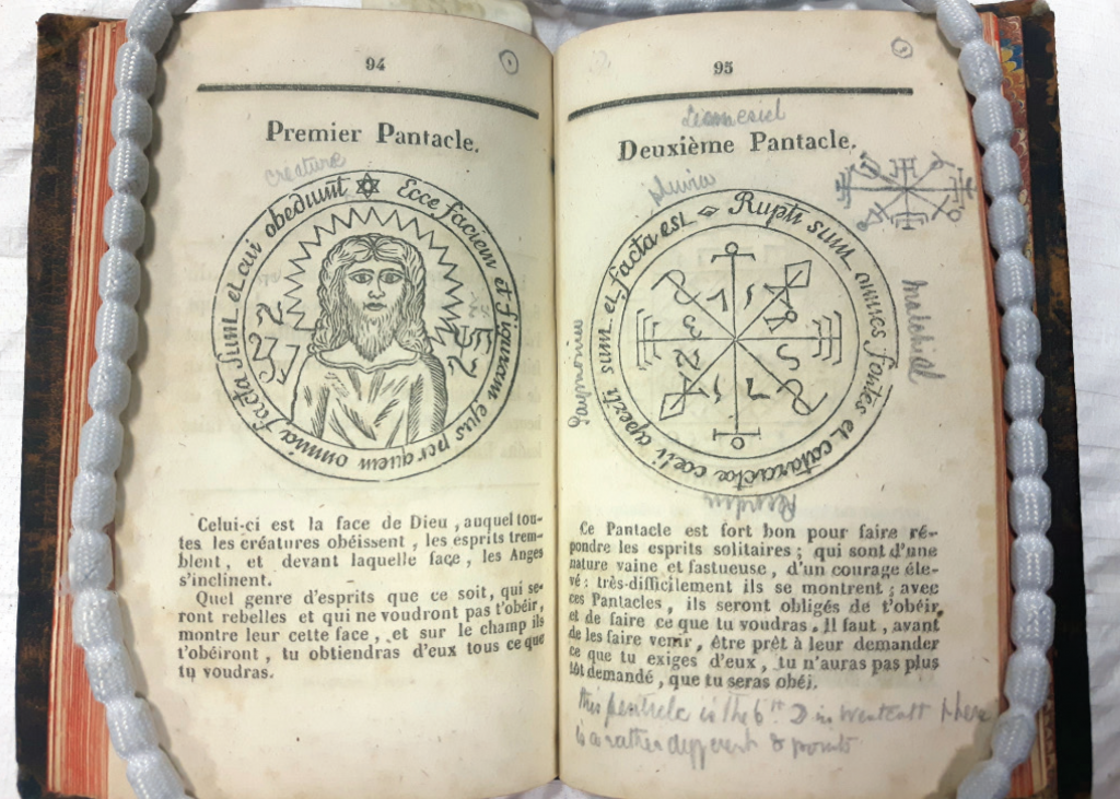 A rare book with aged pages featuring mystical illustrations of pentacles, French-language text, and handwritten annotations in cursive.