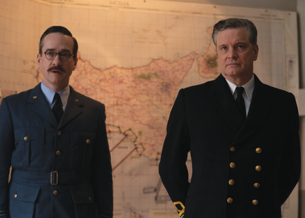 Matthew Macfadyen and Colin Firth dressed in military uniform stand with serious faces in front of a large map of Sicily.