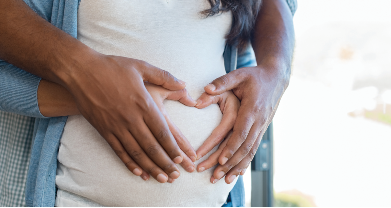 man and woman holding hands on woman's pregnant stomach - forming a heart shape with their hands