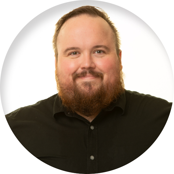 Cameron Wheaton with short brown hair and a trimmed beard wearing a black dress shirt smiling in front of a white background.