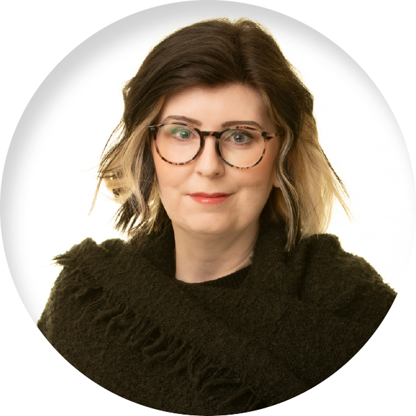 Crystal Mills with brown and blonde hair and glasses wearing a black scarf over a black shirt smiling in front of a white background.