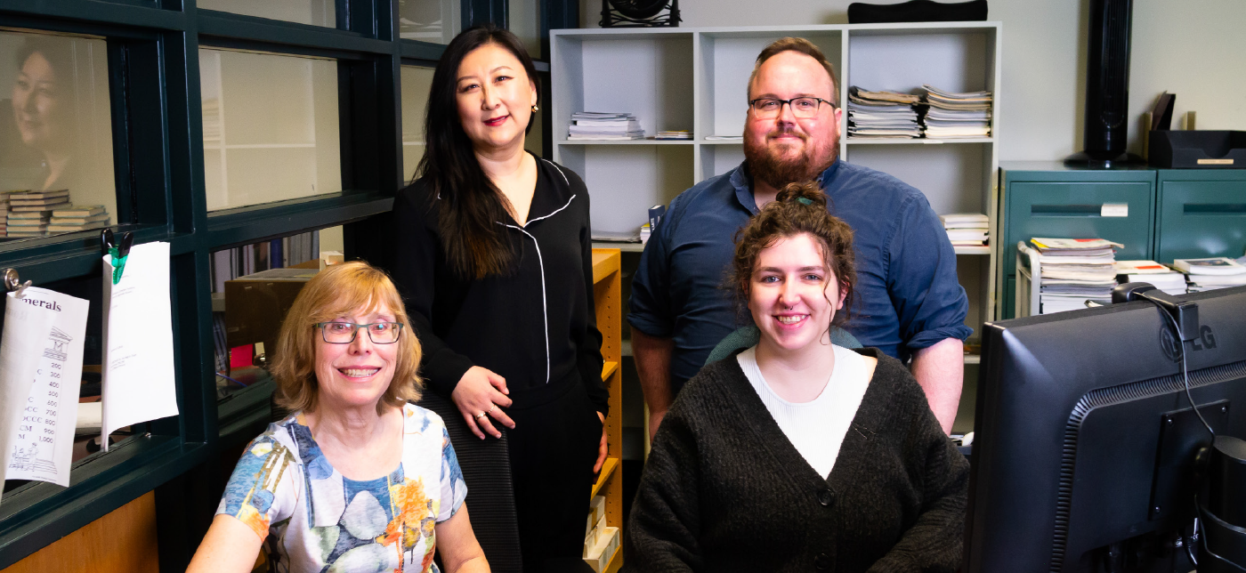 Janice Adlington with long blonde hair, Wei Zhang with long black hair, Cameron Wheaton with short brown hair, and Paige Roman with long curly brown hair, at a desk with books.